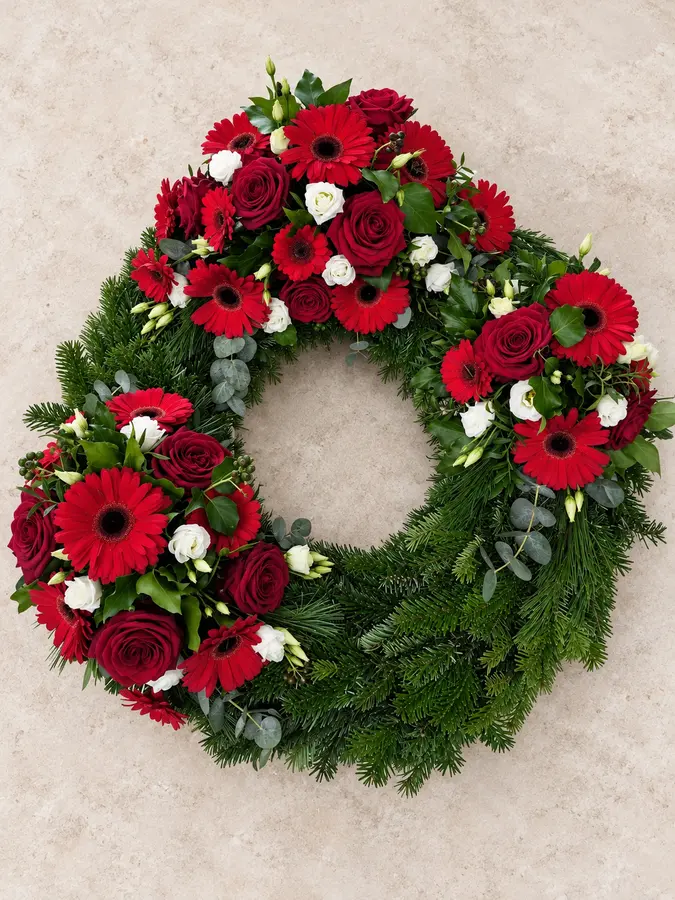 Großer Trauerkranz mit roten Gerbera, dunkelroten Rosen und weißen Blüten